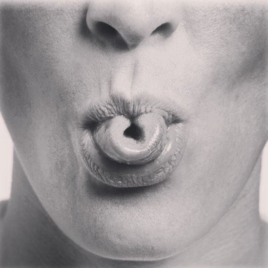Image de la partie basse d'un visage en noir et blanc, la langue est enroulée et sort de la bouche.